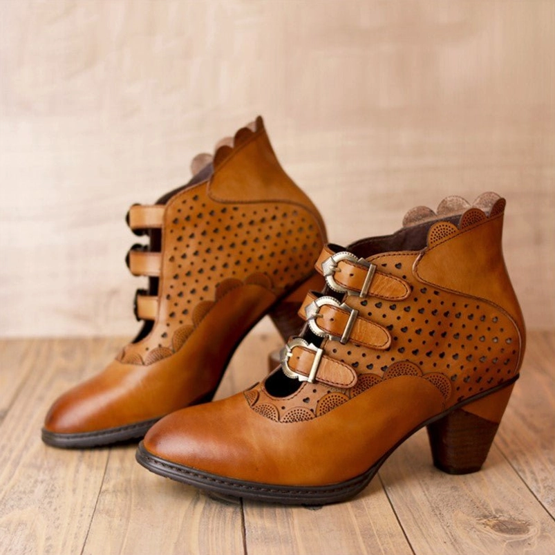 Tan leather steampunk ankle boots featuring triple metal buckle straps, perforated geometric cutout design, and scalloped heel trim shown in front and side profile view