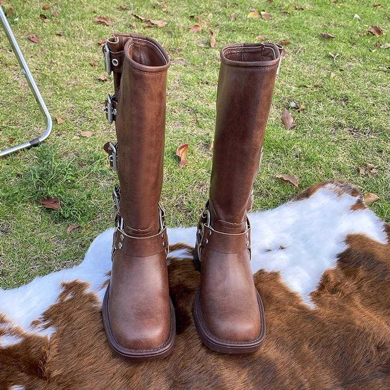 Brown steampunk tall boots with square round toe, block heel, and lower buckle strap, front view on outdoor background