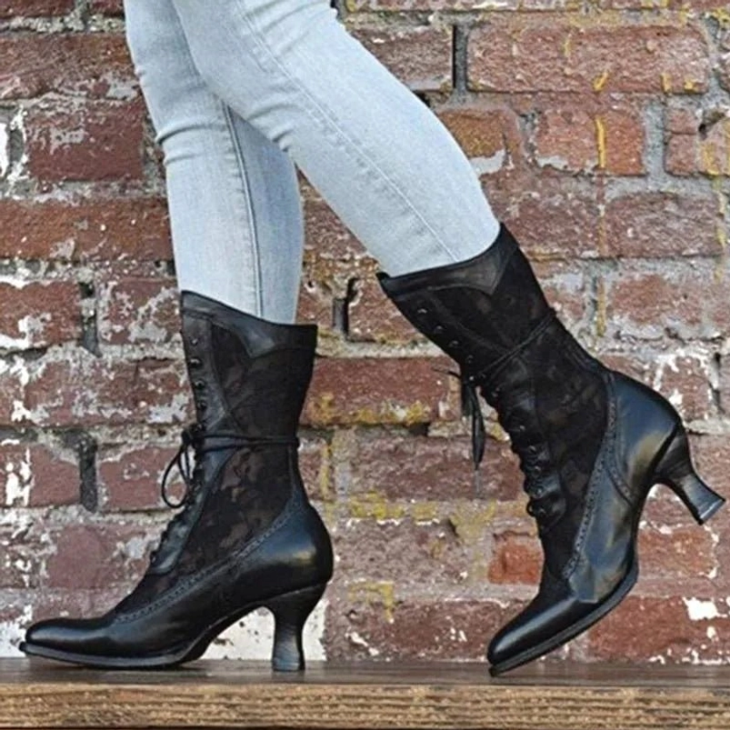 Black Victorian steampunk lace-up boots worn with blue jeans, showing pointed toe and side lacing design against brick wall