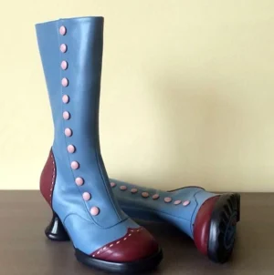 Pair of blue burgundy two-tone steampunk boots with brass button accents displayed on dark surface, front and side view revealing anti-slip rubber outsole, spool heel construction, and premium leather craftsmanship