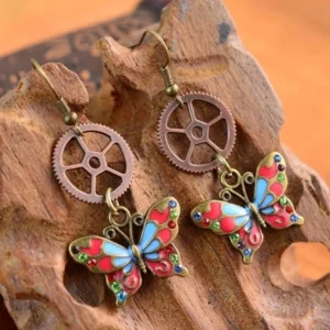 Close-up detail of steampunk butterfly earrings showing reddish-brown vintage metal gears and rhinestone embellished enamel butterfly wings