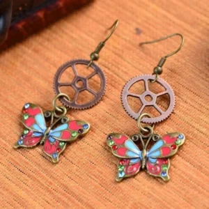 Steampunk butterfly gear drop earrings with antique bronze finish and colorful enamel painted wings displayed on woven bamboo surface