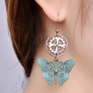 Close-up side view of steampunk butterfly earrings worn on female earlobe with brown hair, displaying detailed craftsmanship and authentic patina finish against light gray backdrop