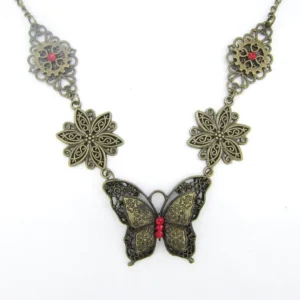 Antique bronze steampunk butterfly necklace with red gemstone pendant, flat lay on white background showing intricate hollow filigree floral design and delicate chain links