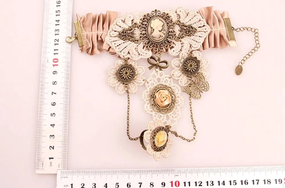 Steampunk cameo wrist accessory flat lay showing dusty pink ruched satin strap, bronze metal charms, cameo lace decor, and hanging chain tassels with measurement reference