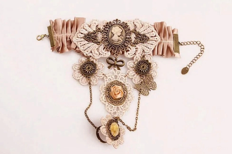 Steampunk hand accessory top-down flat lay featuring ruched dusty pink satin band, vintage bronze hardware, lace cameo ornament, and delicate chain dangles