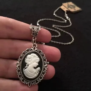 Steampunk cameo necklace with silver filigree metal frame and vintage black-and-white lady portrait, displayed on dark fabric with intricate metalwork details visible in close-up side view