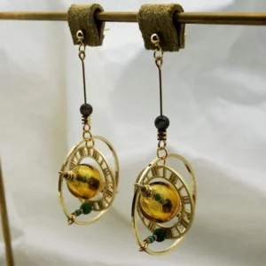 Steampunk celestial orbit earrings with amber glass center bead and green-brown accent beads, displayed on gold metal rod with white backdrop