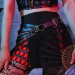 Gothic steampunk leather chain belt with layered dual straps and silver metal rivets, front-facing waist view paired with red plaid skirt, displaying linked chains and studded industrial details