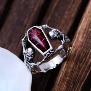 Gothic steampunk coffin ring featuring dual skeleton frames around central coffin motif with dark patterned details on dark wooden surface - three-quarter side view