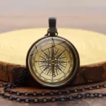 steampunk compass necklace with black metal frame and glass compass dial displayed on wooden surface, vintage navigation design