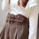 Steampunk corset belt worn by model showing dual bronze buckles and distressed brown leather, side profile waist view demonstrating silhouette-defining wide waist design and industrial hardware aesthetic
