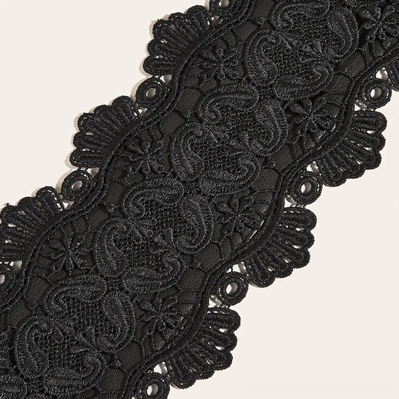 Flat lay detail shot of black steampunk corset belt displaying full scalloped lace edge, floral paisley embroidery, and lace texture on white background