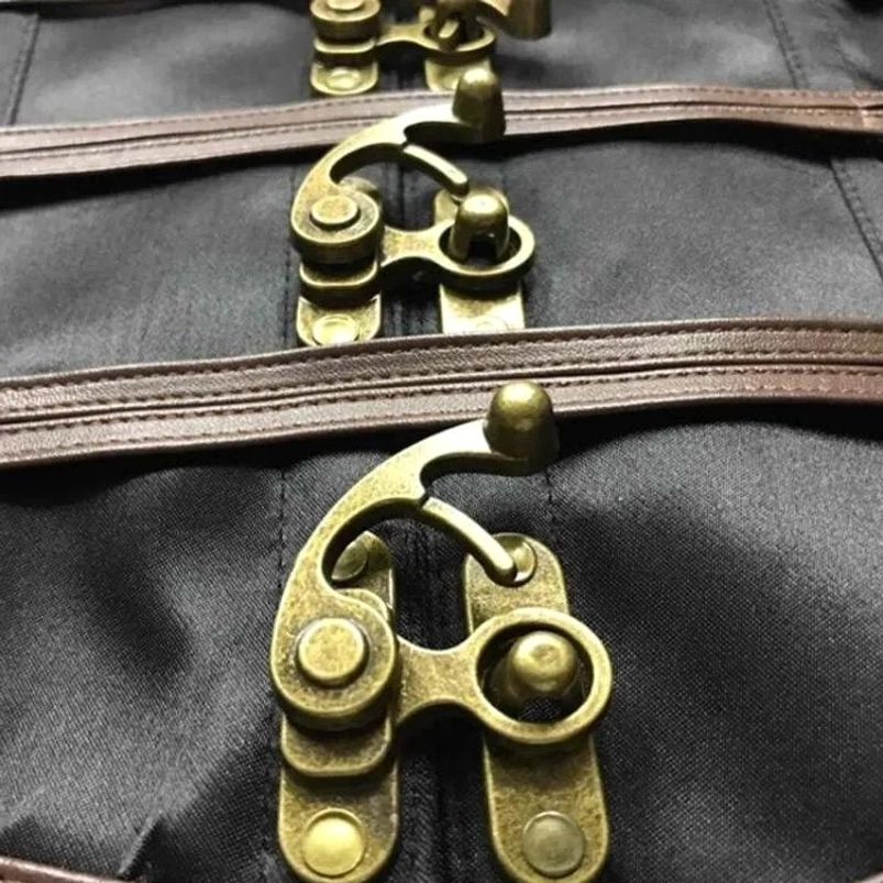 Close-up macro detail of steampunk corset hardware featuring antique bronze toggle clasps, brown leather straps and black satin fabric