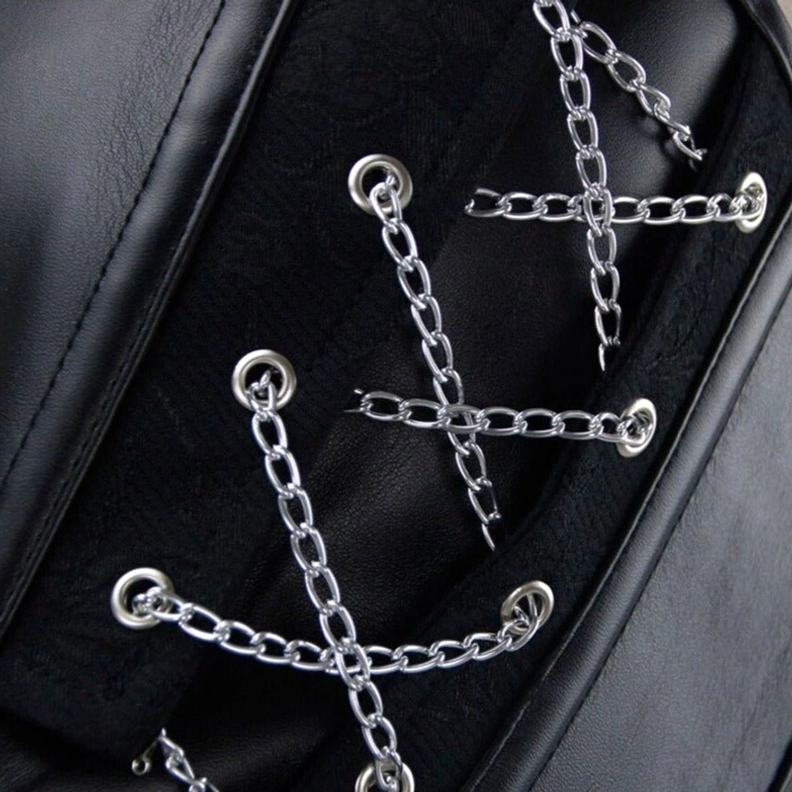 Close-up macro detail of steampunk corset showing silver cross chain ornaments, metal eyelets, and mixed leather jacquard texture