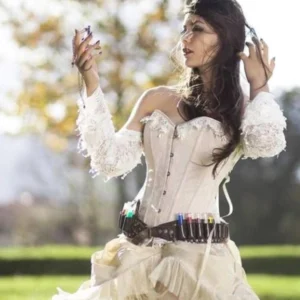 Steampunk corset outfit styled on model in outdoor setting with beige corset, lace sleeves, utility waist belt with test tubes, and ruffled skirt for complete vintage aesthetic