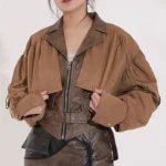 Two-tone steampunk cropped leather jacket front view with khaki and dark brown color blocking, adjustable waist belt, and notched lapel design worn by female model