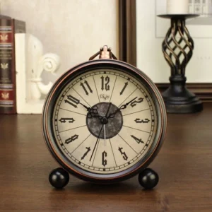 Steampunk desk clock direct front view showcasing aged off-white dial with hand-applied Gothic numerals, black metal frame with bronze trim, and decorative spherical feet