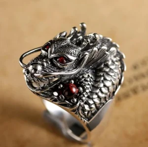 Steampunk silver dragon ring front-left close-up view showing detailed scaled texture, red gem eyes, and antique silver finish on vintage paper background