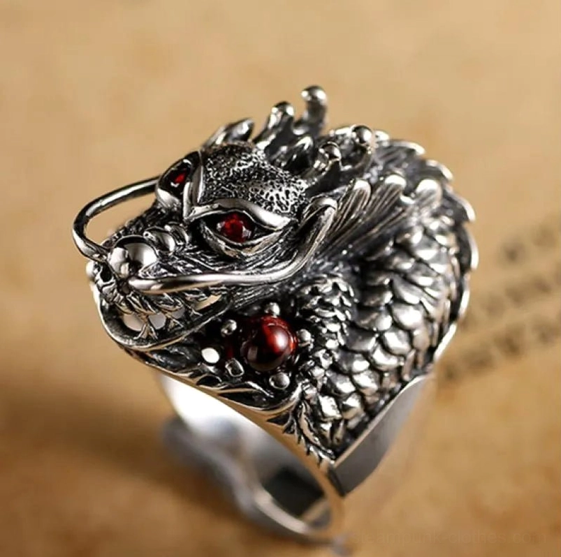 Steampunk silver dragon ring front-left close-up view showing detailed scaled texture, red gem eyes, and antique silver finish on vintage paper background