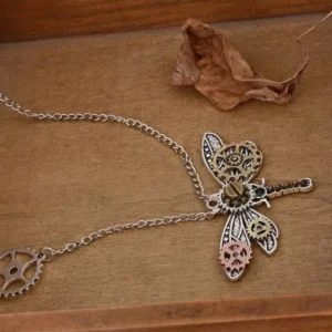 Close-up view of steampunk dragonfly necklace highlighting stainless steel curb chain with gear charm accent and dual-tone metallic finish on wooden surface with dried leaf styling