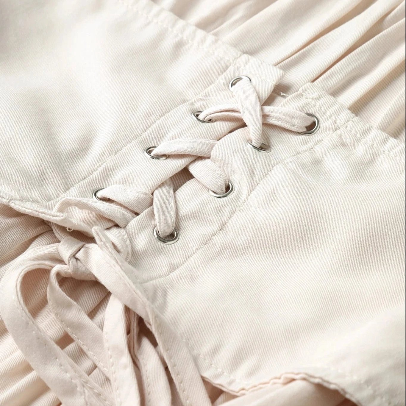Close-up of beige dress lace-up corset waist with metal eyelet fasteners and woven polyester fabric texture showing steampunk-inspired construction
