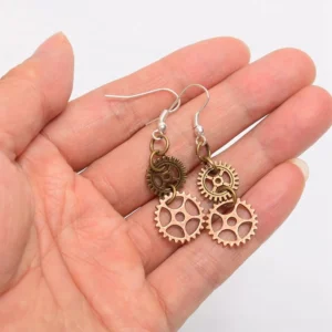 Handcrafted steampunk dual gear earrings held in palm, close-up detail view showing silver ear hooks and mixed bronze-gold patina tones