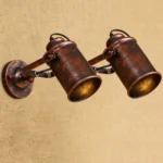 Dual-head steampunk wall lamp with adjustable swing arms, distressed bronze iron finish, front three-quarter view showing articulated joints and mechanical design