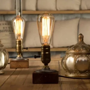 Vintage Edison bulb steampunk table lamp with spiral filament and aged bronze metal socket, showing warm incandescent glow on wooden base