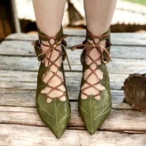Green steampunk elf pointed lace-up flats with leaf-shaped cutout design, front view on outdoor wooden deck