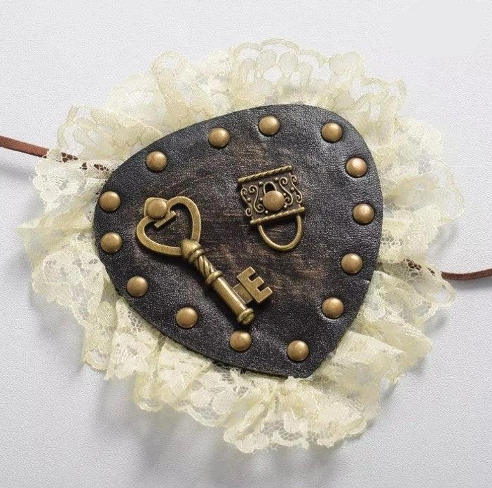 Steampunk Lolita eye patch top-down close-up showing black leather base brass rivets heart-shaped key ornament and cream lace detailing