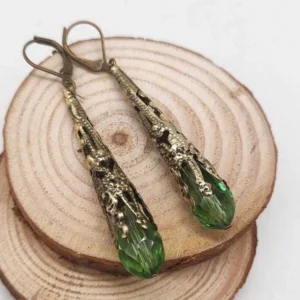 Steampunk teardrop dangle earrings with green faceted crystal and antique bronze filigree metal, displayed on wooden coaster with white background