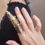 Steampunk articulated finger armor with mixed vintage gold and silver finish displaying hollow carved design and dotted textured surface worn on female hand in close-up side view