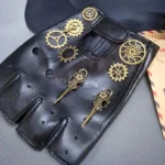 Black fingerless steampunk biker gloves with brass gear and key pendants, flat lay top-down view