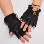 Black fingerless steampunk gloves with golden gear ornament and ruffled lace cuffs on female model hands, front view studio shot