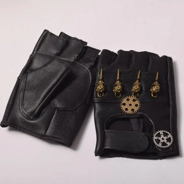 Black fingerless steampunk leather gloves with brass skull and gear ornaments, flat lay top-down view on white background