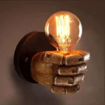 Steampunk fist wall sconce with wood-textured resin hand and dark metal mount, featuring warm Edison bulb in close-up studio view