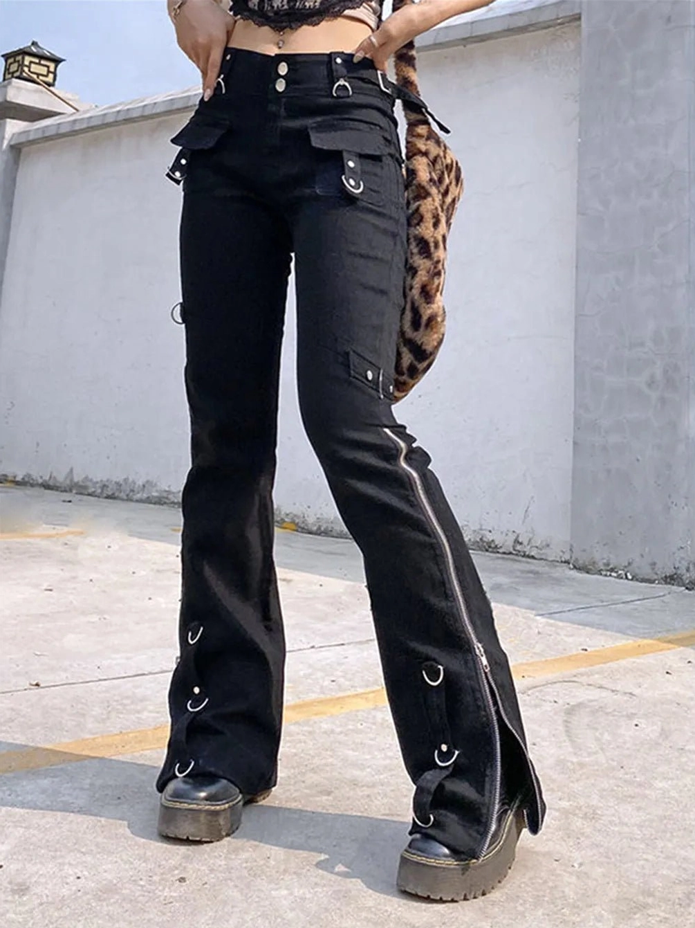 Black steampunk flared cargo trousers front view with side zippers, metal eyelets, D-rings and buckle details - female model wearing alternative gothic pants with platform boots