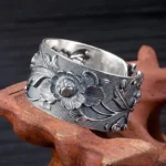 Vintage steampunk floral ring with deep relief peony carving, adjustable sterling silver band on wooden display stand, three-quarter view