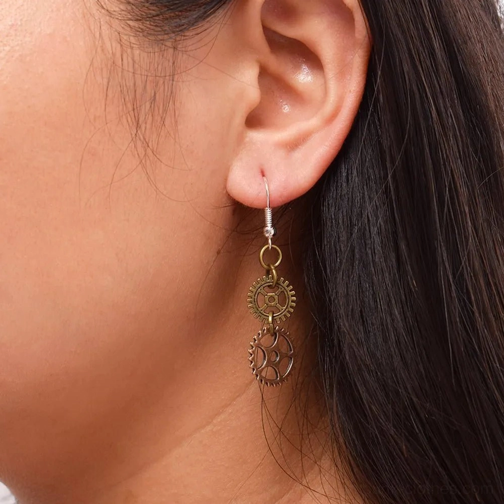 Woman wearing steampunk dual gear drop earrings, side profile close-up showing hanging double-gear design in bronze tones worn on ear