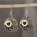 Steampunk gear heart drop earrings with vintage mixed metal finish and rose-gold accents, hung on wooden branch against dark background