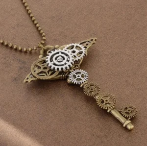 Steampunk gear key pendant necklace featuring mixed bronze and silver tonal metal gears with ball bead chain, displayed on brown fabric from overhead side angle