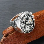 Steampunk mechanical gear ring with antique silver finish and gold accents, shown from oblique side-front view against dark wooden background