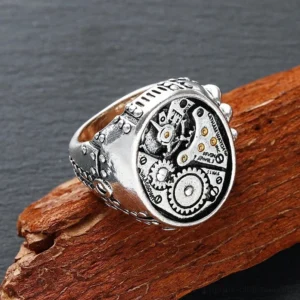 Steampunk mechanical gear ring with antique silver finish and gold accents, shown from oblique side-front view against dark wooden background