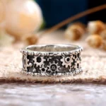 Steampunk carved gear ring top-down close-up view showing intricate hollow gear patterns, rivet edge trim, and vintage silver metal finish with aged blackened texture on burlap and wooden surface