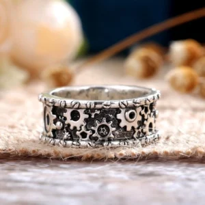 Steampunk carved gear ring top-down close-up view showing intricate hollow gear patterns, rivet edge trim, and vintage silver metal finish with aged blackened texture on burlap and wooden surface