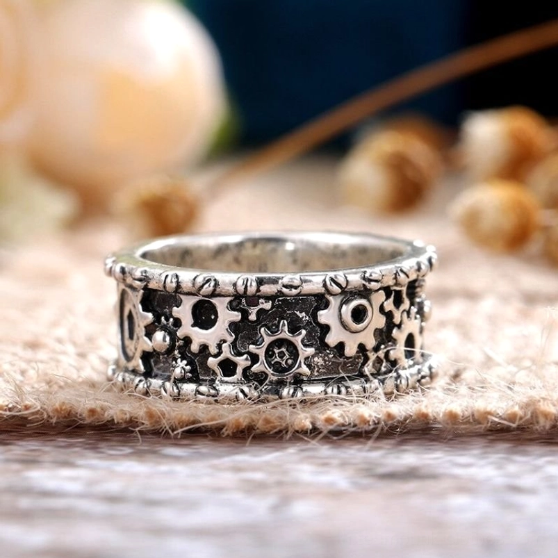 Steampunk carved gear ring top-down close-up view showing intricate hollow gear patterns, rivet edge trim, and vintage silver metal finish with aged blackened texture on burlap and wooden surface