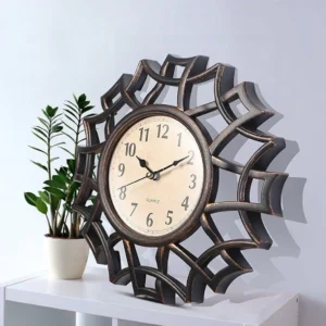 Steampunk geometric wall clock with dark bronze web-style frame displayed on home interior shelf with potted plant, three-quarter view showing dimensional hollow design