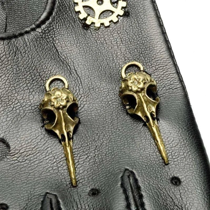 Macro close-up detail of steampunk glove showing brass raven skull pendants and gear accents