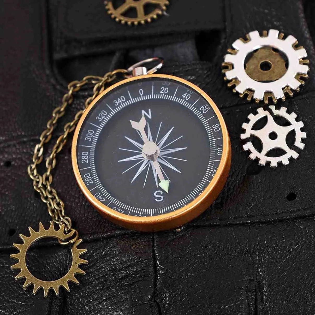 Macro close-up of steampunk glove compass detail featuring brass and white metal gears, chain-attached directional compass with precision scale markings on black leather